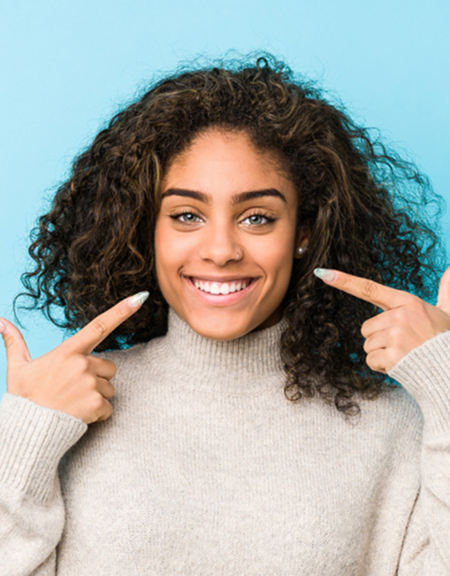 Smiling woman pointing at her teeth while standing against a blue background