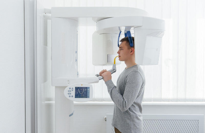 Patient standing in a dental clinic undergoing a 3D panoramic X-ray scan for orthodontic diagnosis